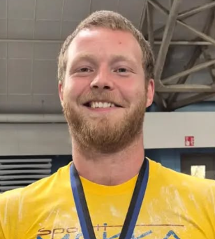 Man wearing a yellow shirt with a logo, standing indoors. | Strom Sports Supplements NZ